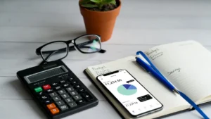 Flat lay of calculator, notebook with budget, smartphone with banking app, and glasses, representing UK financial planning for loans.