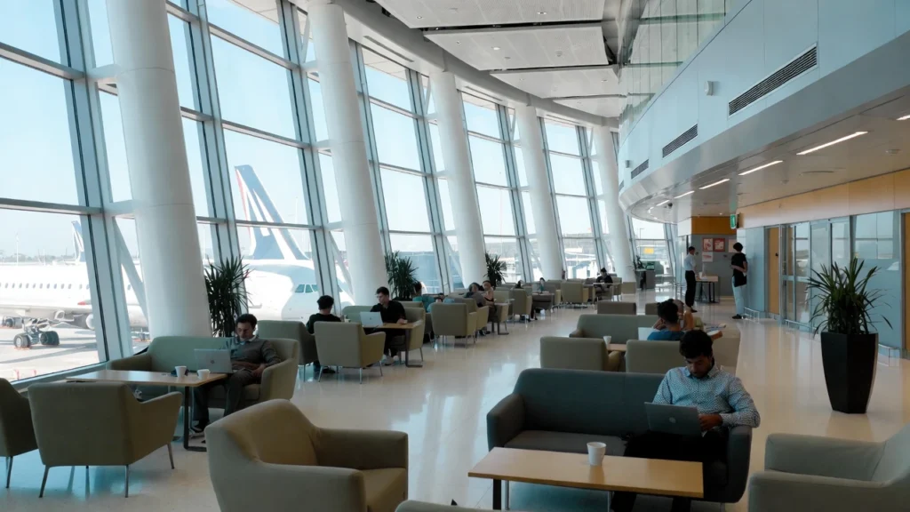 Modern airport lounge with travellers relaxing, using laptops, and enjoying refreshments.
